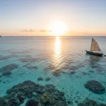 Clear shallow reef water in Belize with a small boat nearby.